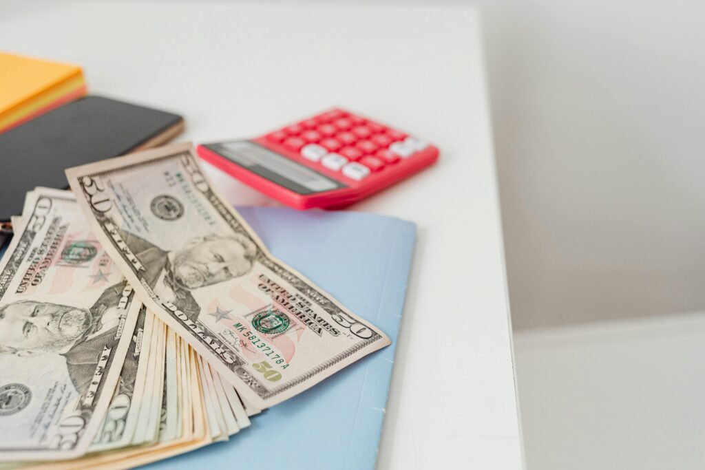 pexels-photo-7680697-7680697 Close-up of notebooks, US dollars, and a calculator on a desk.